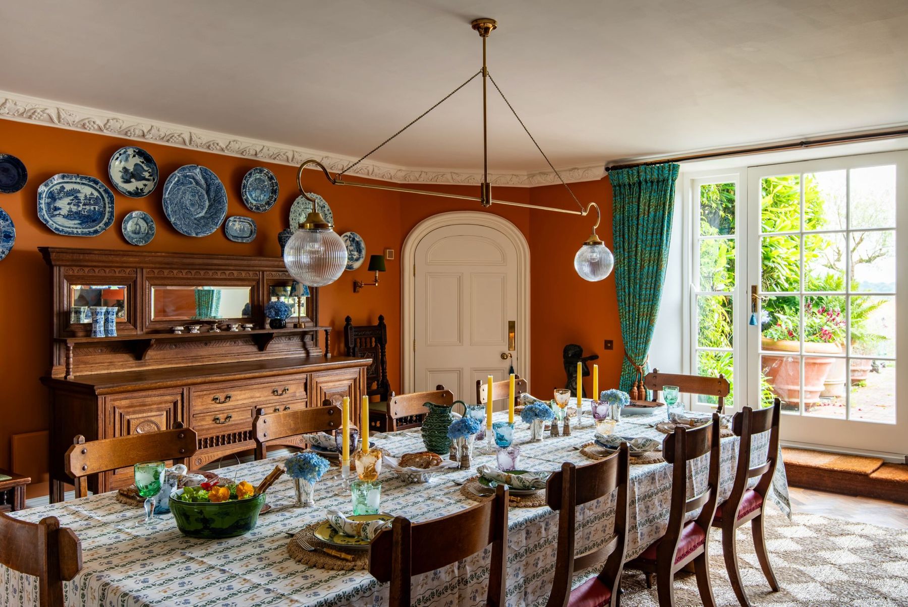 The dining room, with burnt-orange walls, blue-and-white plates and a long laid table