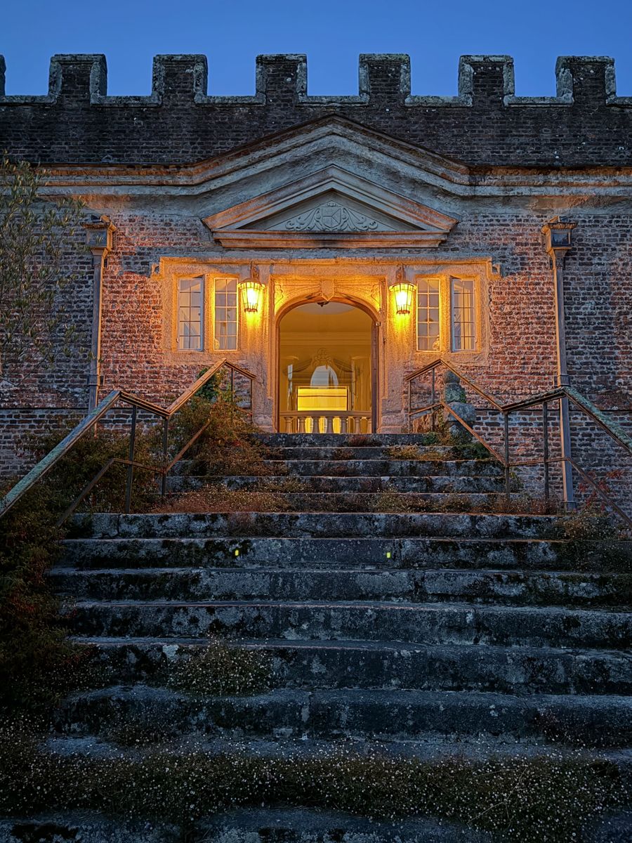 The front steps and pedimented doorway lit at dusk beneath the battlements