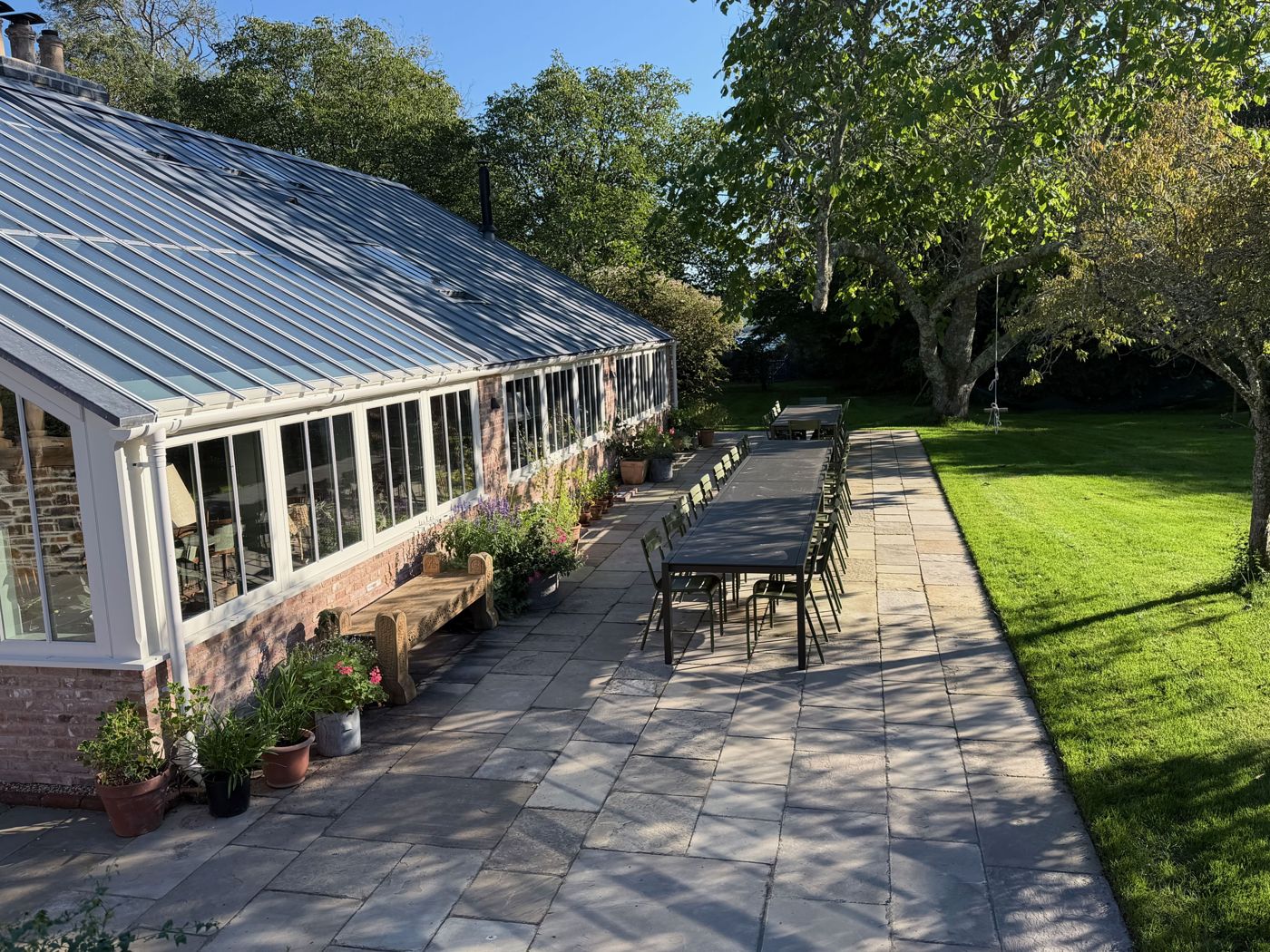 The long glasshouse beside the lawn, with a table laid outside